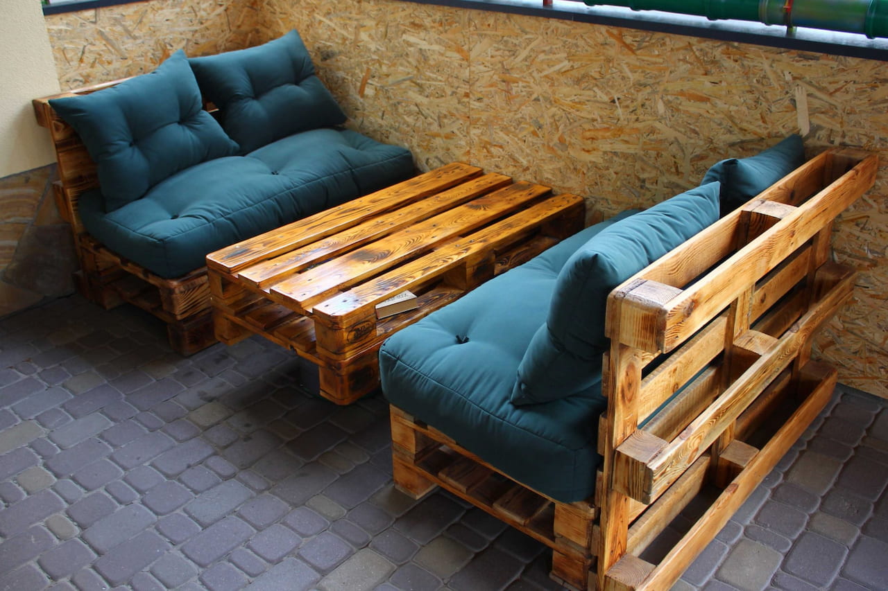 Два кресла и стол из деревянных поддонов покрытых лаком и украшенных подушками.